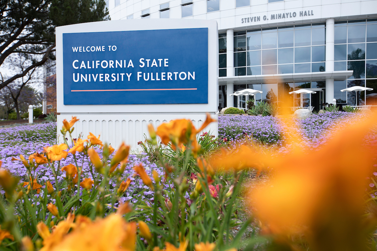 Sign reading "Welcome to California State University Fullerton" in front of the Steven G. Mihaylo Hall building with gardens.