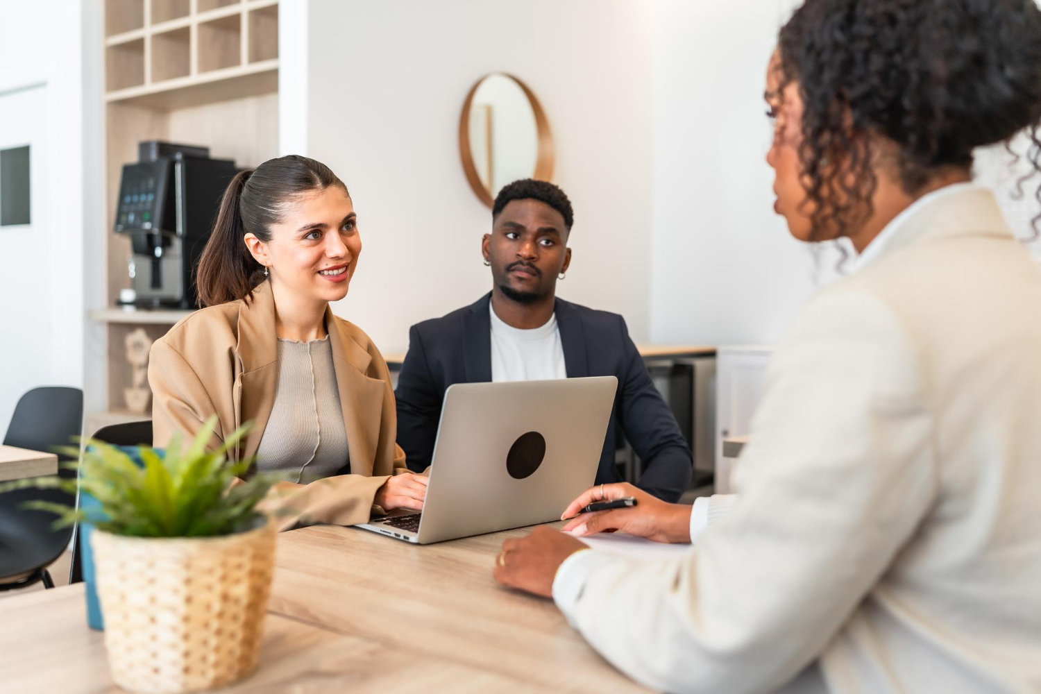 Three people in a professional setting having a conversation with a laptop on the table.