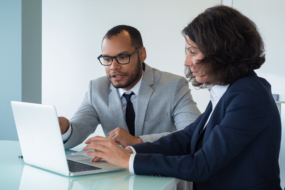 a man and a woman looking at the screen of a laptop