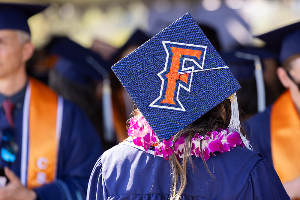 a person wearing graduation blue robe with a blinged out graduation cap with the letter "F"