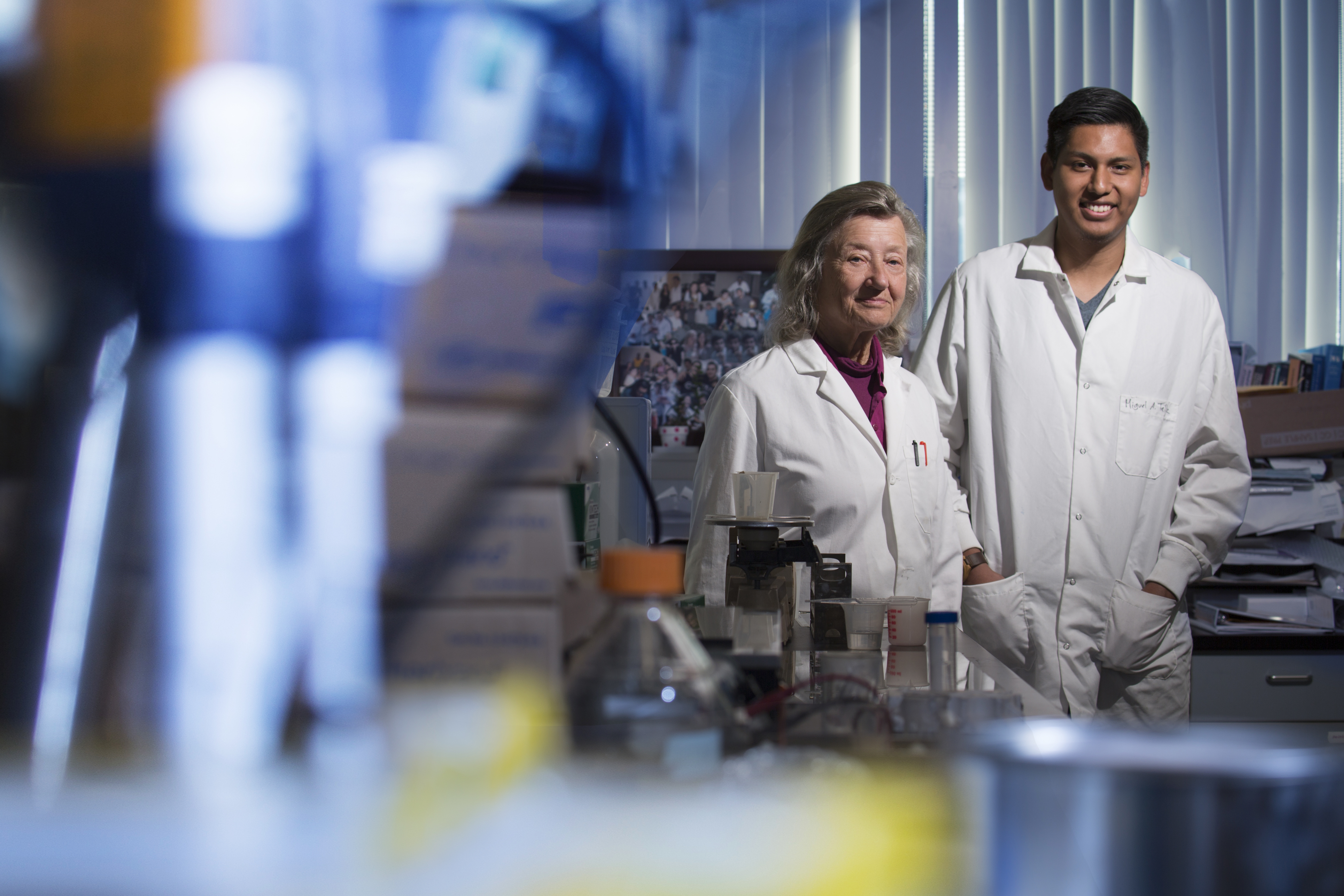 an older lady and a young man standing next to each other in lab coats